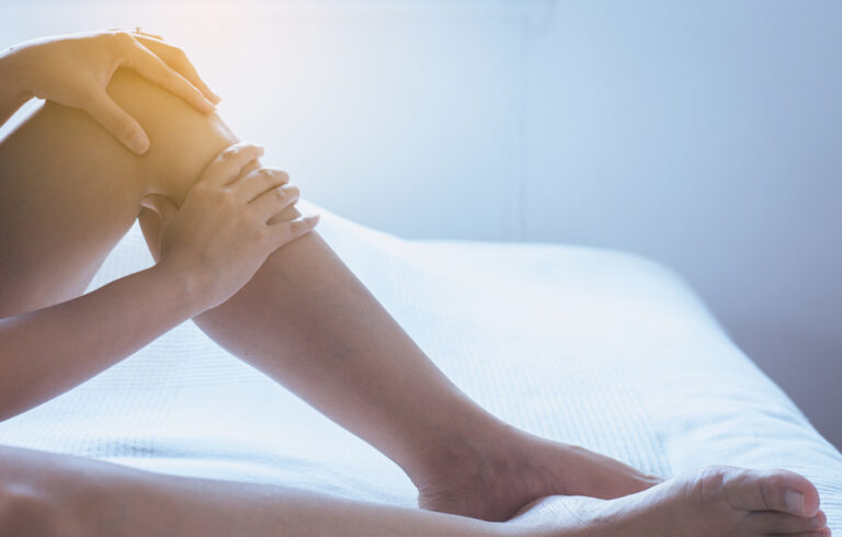 Patient laying in bed and touching their leg in pain from a venous ulcer as a result of venous insufficiency.